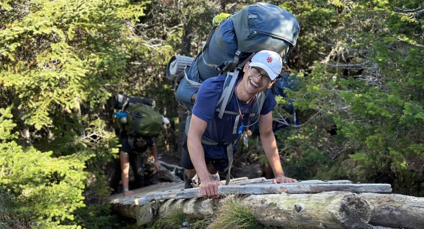 A person wearing a backpack makes their way over a ladder